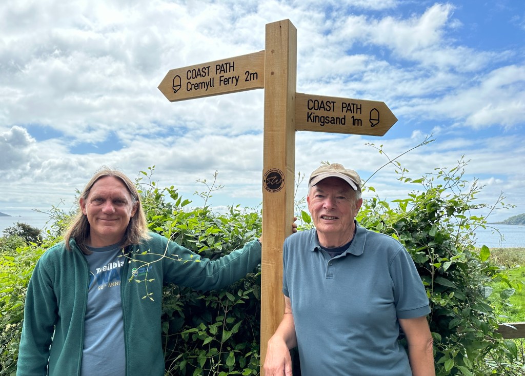 John and Julian walking at the Rame peninsula on the South West Coast Path, where a sign has been placed in memory of John's wife Carol