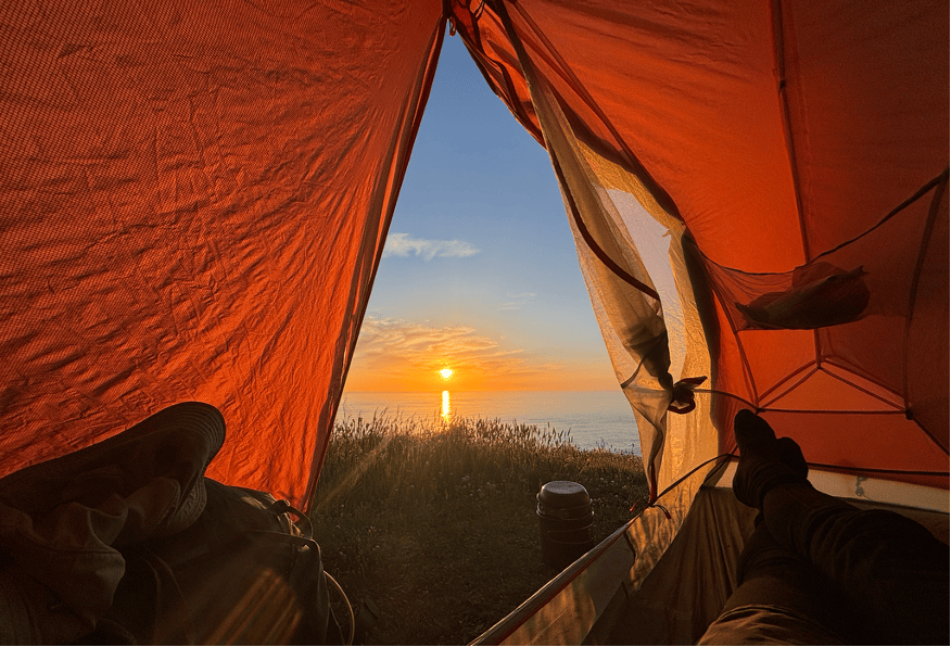 View from inside a tent at sunrise, with a scenic view of the sun rising over a calm body of water.